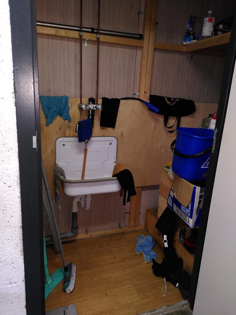 Opgeruimd werkhok met schoonmaakmiddelen, dweil en emmer in de dojo van SJOK